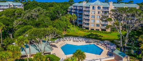 A hotel with a large pool surrounded by lush greenery and a view of the ocean.