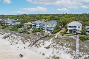 A beachfront property with multiple houses, a wooden walkway, and a sandy beach. - Stunning oceanfront home with pool, private boardwalk, decks, & elevator (Hilton Head)