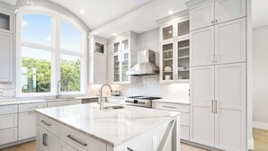 Cocina moderna con armarios blancos, una isla grande, estufa y ventana con vista a follaje.