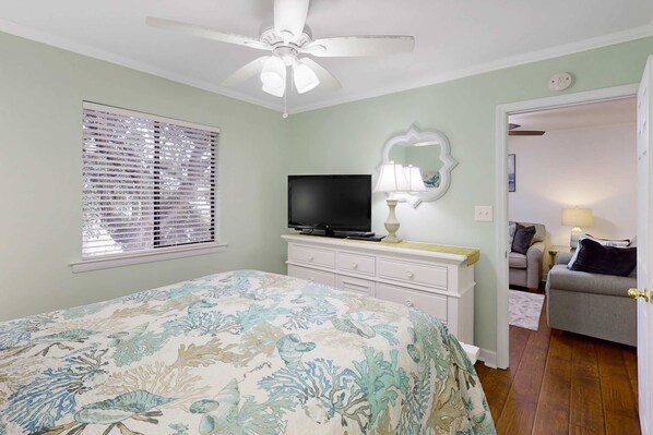 A bedroom with a bed, a television, a dresser, a mirror, and a door leading to another room. - Top floor Fiddlers Cove condo with resort pools, hot tub & beach access (Hilton Head)