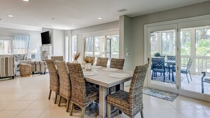 Een ruime eethoek met een grote tafel en rieten stoelen, een keuken met een flatscreen televisie, en een balkon met zitgelegenheid.
