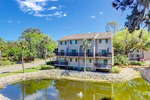 A multi-story hotel with balconies, a pond, and surrounding greenery. - Beautiful villa, family friendly with balcony, beach access, pool, & washer dryer (Hilton Head)