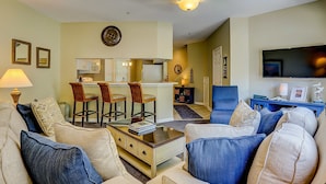 A living room with a sofa, chairs, a coffee table, a TV, and a kitchen area with a dining table and chairs. - Dog-friendly island escape near the beach with pool, water view & WiFi (Hilton Head)