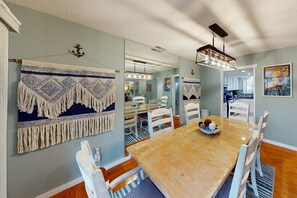 A dining area with a wooden table, white chairs, and a hanging light fixture. - Relaxing Coastal Escape- Golf course view with shared pool, nearby beach access, and serene island charm (Hilton Head)