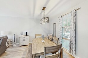 A dining area with a wooden table, chairs, a hanging light fixture, a cabinet, and a window with patterned curtains. - Lagoon View Villa 2 Pools walk to beach & shops (Hilton Head)