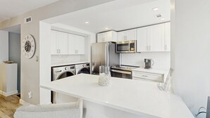 Una cocina moderna con armarios blancos, un refrigerador de acero inoxidable, un microondas y un horno empotrado.