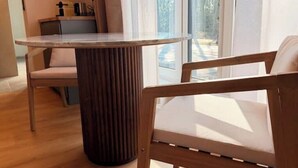 A dining area with a round table, a wooden chair, and a view through large windows. - Villa Weitmar: Private spa - sauna and designer bathtub (Bochum)