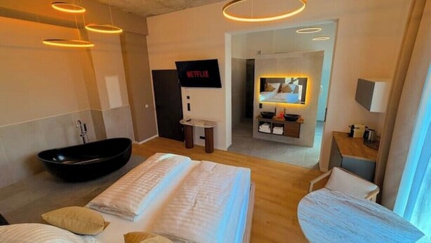 A modern hotel room with a large bed, a bathtub, a small desk, and a TV. - Villa Weitmar: Private spa - sauna and designer bathtub (Bochum)