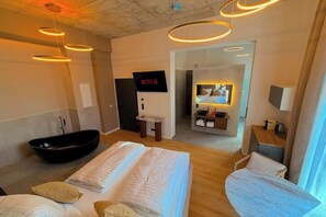 Une chambre d’hôtel moderne avec un grand lit, une baignoire, un petit bureau et un téléviseur.