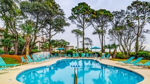 Ein Pool mit Liegestühlen und Sonnenschirmen, umgeben von Bäumen und Gebäuden.