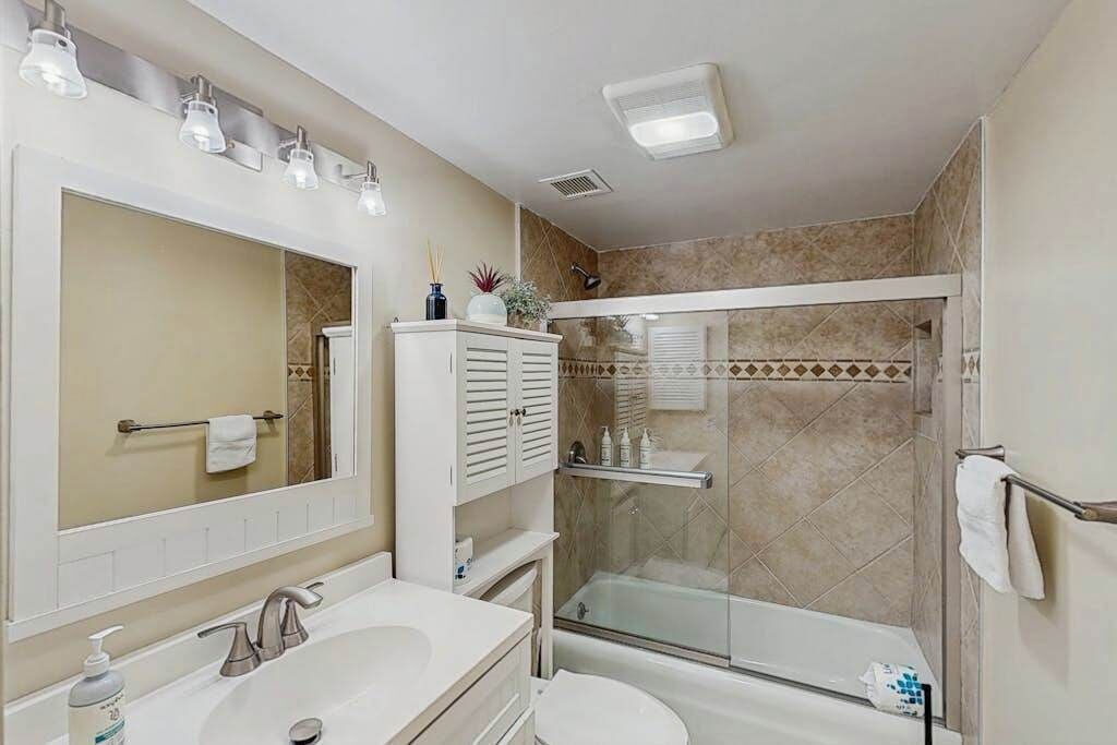 A bathroom with a large mirror, a sink, a toilet, a shower with a glass door, and a towel rack.