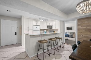 Een moderne keuken met witte kasten, een centraal keukenblok met krukken, een eettafel en een kroonluchter.