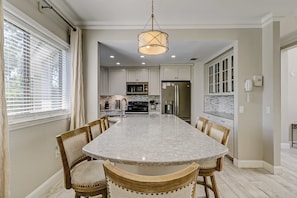 A kitchen with a central island, wooden chairs, and a hanging light fixture. - Walk to the beach Top-floor penthouse with 4 balconies & pool (Hilton Head)
