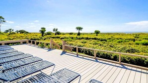 Una terraza con sillones de sol que da a un jardín cuidado con árboles pequeños y un cielo despejado.