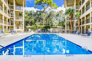 A swimming pool with blue lane dividers, surrounded by lounge chairs and palm trees, with a multi-story building in the background. - Updated Condo with Fast WiFi, Shared Pool, Balcony & Central AC - Walk to Beach (Hilton Head)