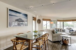 A modern living room with a glass dining table, wicker chairs, a sofa, and a large framed picture on the wall. - Yacht Club Villas Updated corner condo with marina view, shared pool & hot tub (Hilton Head)