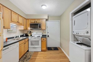 A compact kitchen with wooden cabinets, a microwave, stove, dishwasher, and a washing machine.