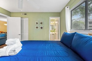 A bedroom with a blue bed, white towels, a wardrobe, and a window with blinds.