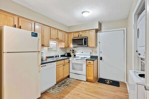 A compact kitchen with wooden cabinets, a white refrigerator, a microwave, a stove, and a dishwasher.