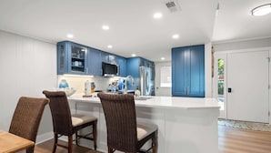 Una cucina moderna con mobili bianchi, un'isola centrale e un'area pranzo con sedie in vimini.