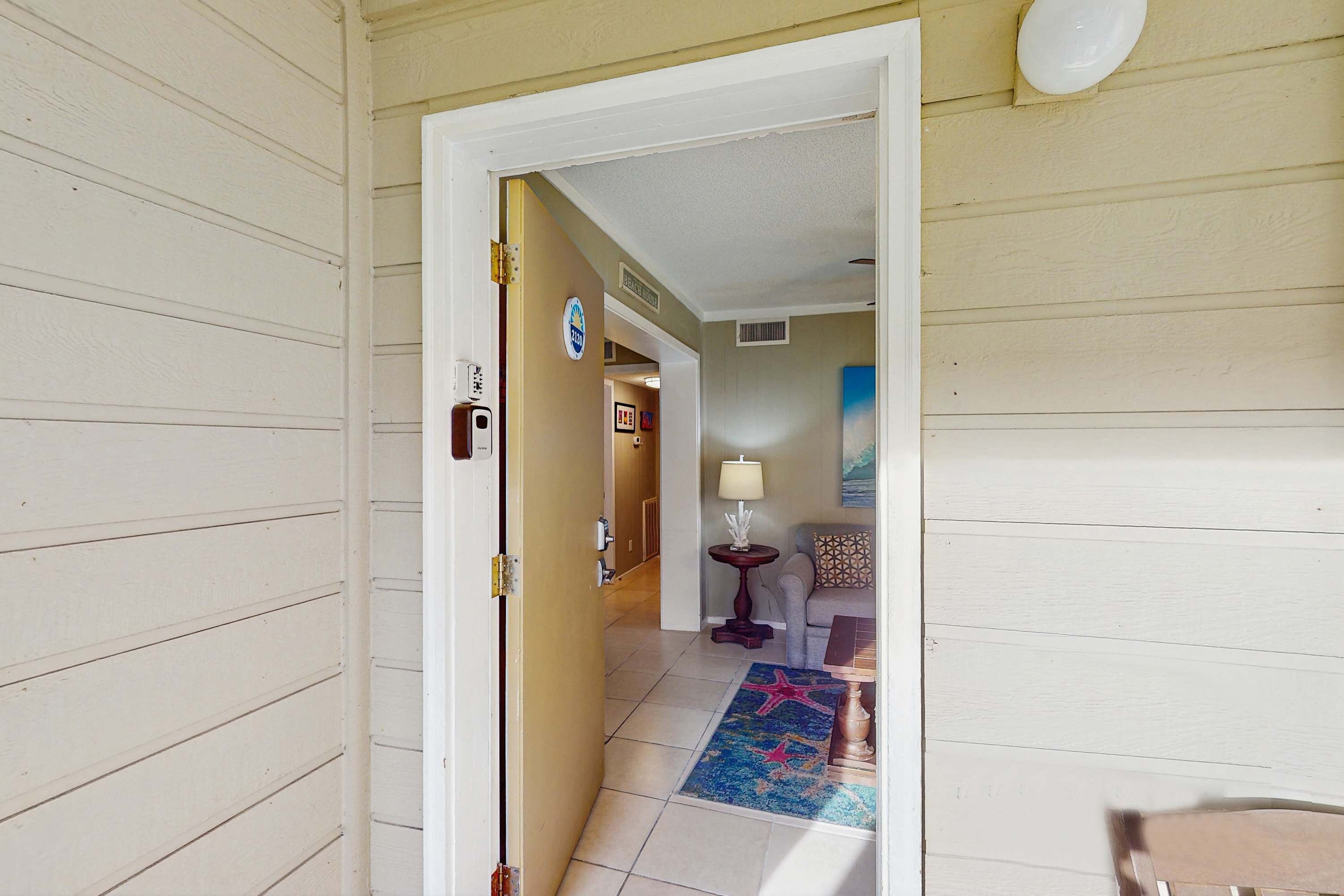 A hallway with a door leading to a room, a lamp, a star-patterned rug, and a chair.