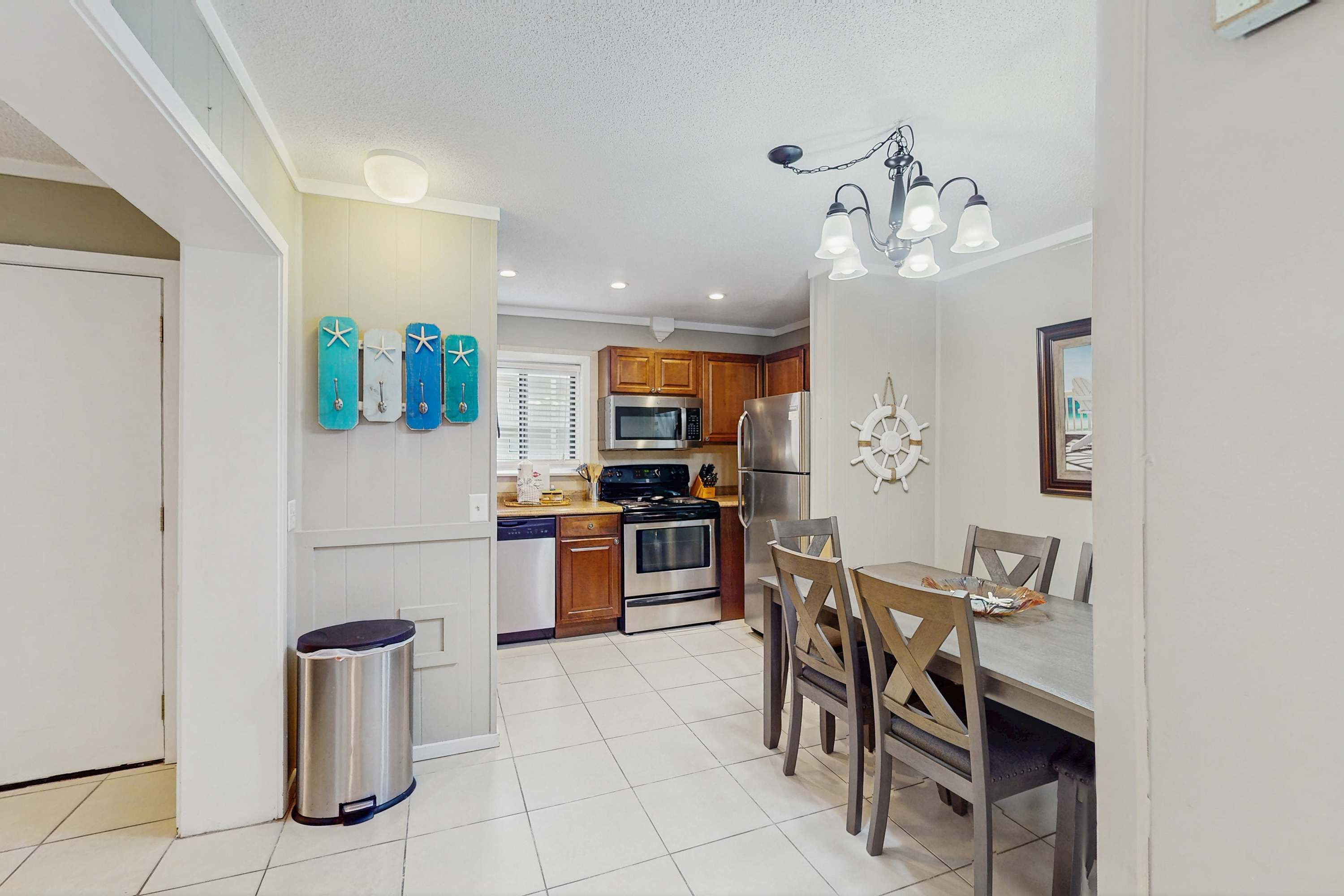 A compact kitchen with modern appliances, a dining area with wooden chairs, and a small trash bin.