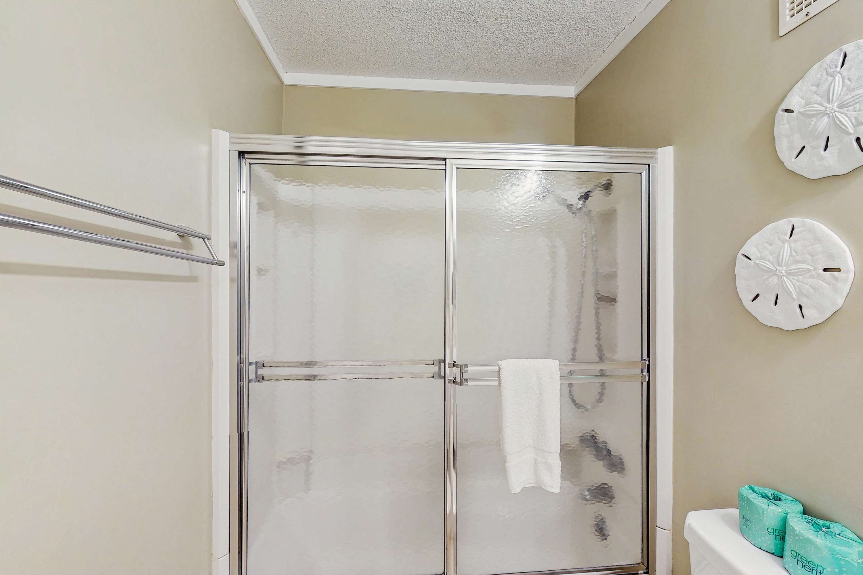 Un baño con cabina de ducha de vidrio, un perchero para toallas y un inodoro con papel higiénico verde.