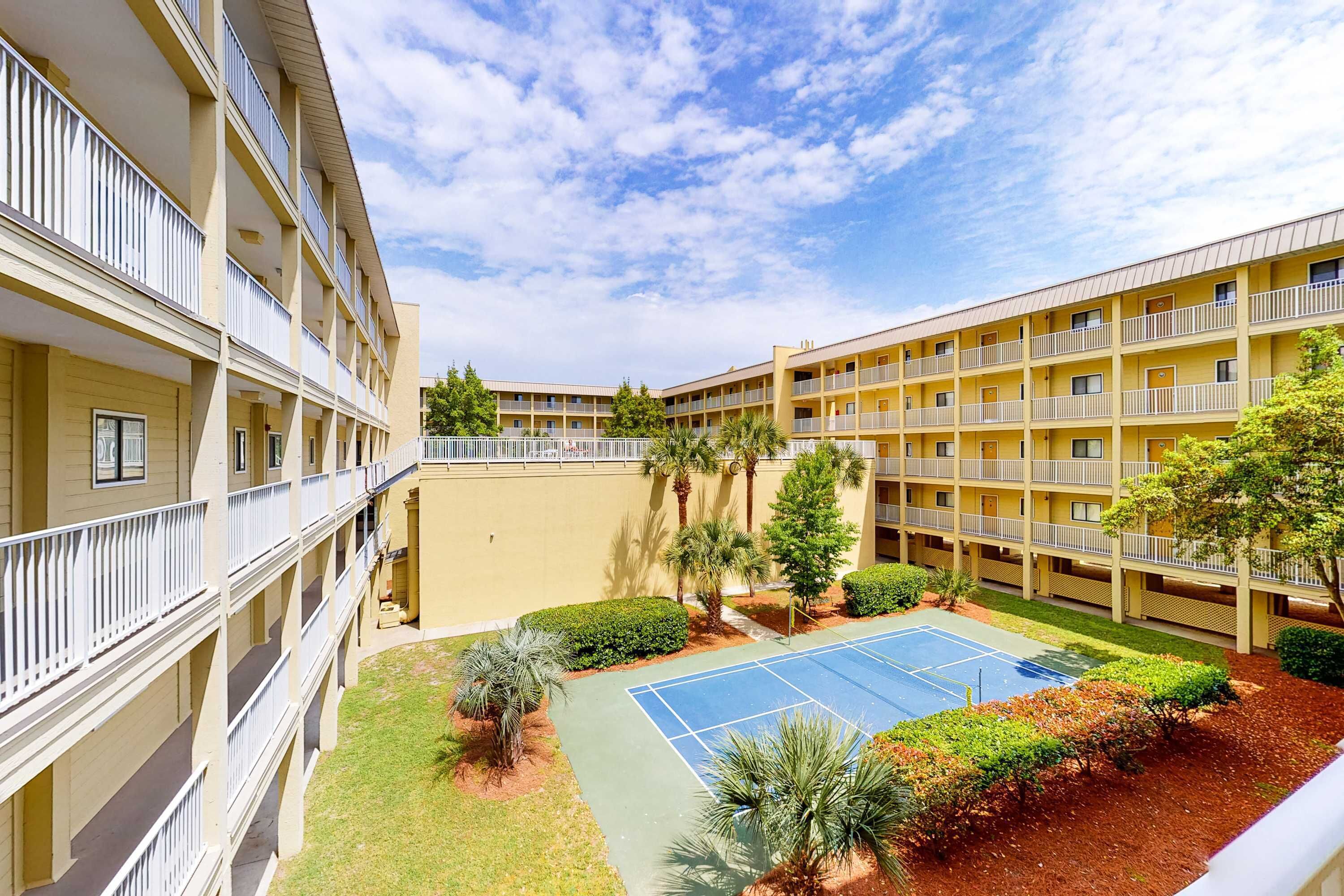 A multi-story hotel with balconies, a tennis court, and landscaped areas.
