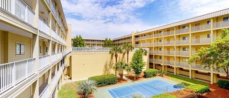 A multi-story hotel with balconies, a tennis court, and landscaped areas.