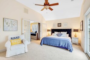 A bedroom with a bed, a chair, a ceiling fan, and a door leading to another room. - Spacious Deck, Hot Tub,  Second Row To Beach & Brand New Private Pool & Spa (Hilton Head)