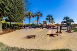 A sandy outdoor area with wooden benches, a gazebo, palm trees, and a playground. - Island oasis with balcony, beach access, pool, hot tub (Hilton Head)