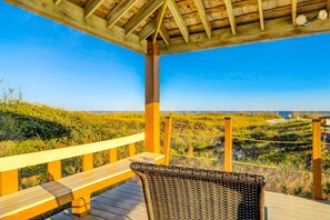 Une terrasse en bois avec un fauteuil en osier, donnant sur un paysage côtier.