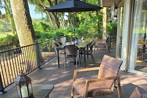 Um deck de madeira com móveis de exterior, uma mesa e cadeiras, cercado por grades e árvores.