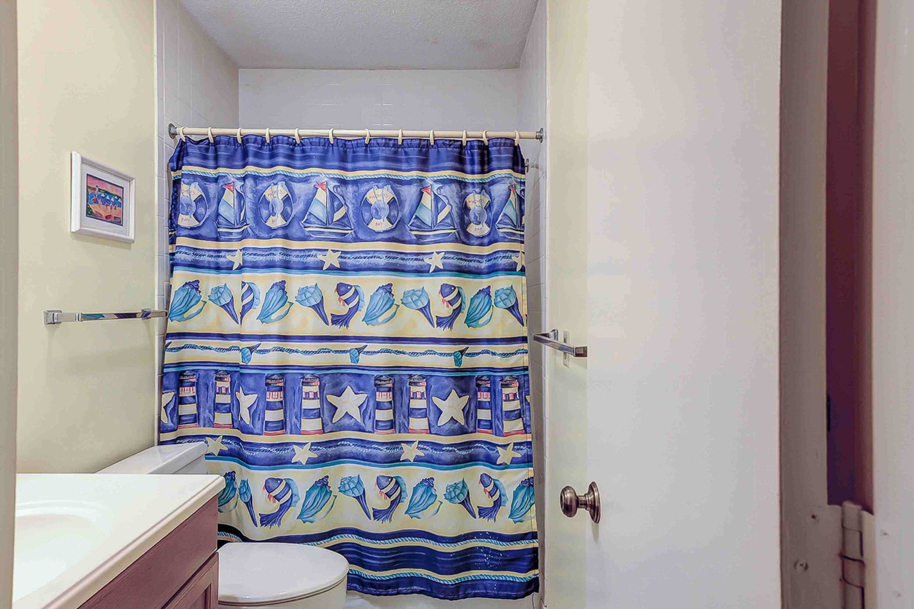 Une salle de bain équipée d’un rideau de douche orné de motifs marins, de toilettes et d’un lavabo.