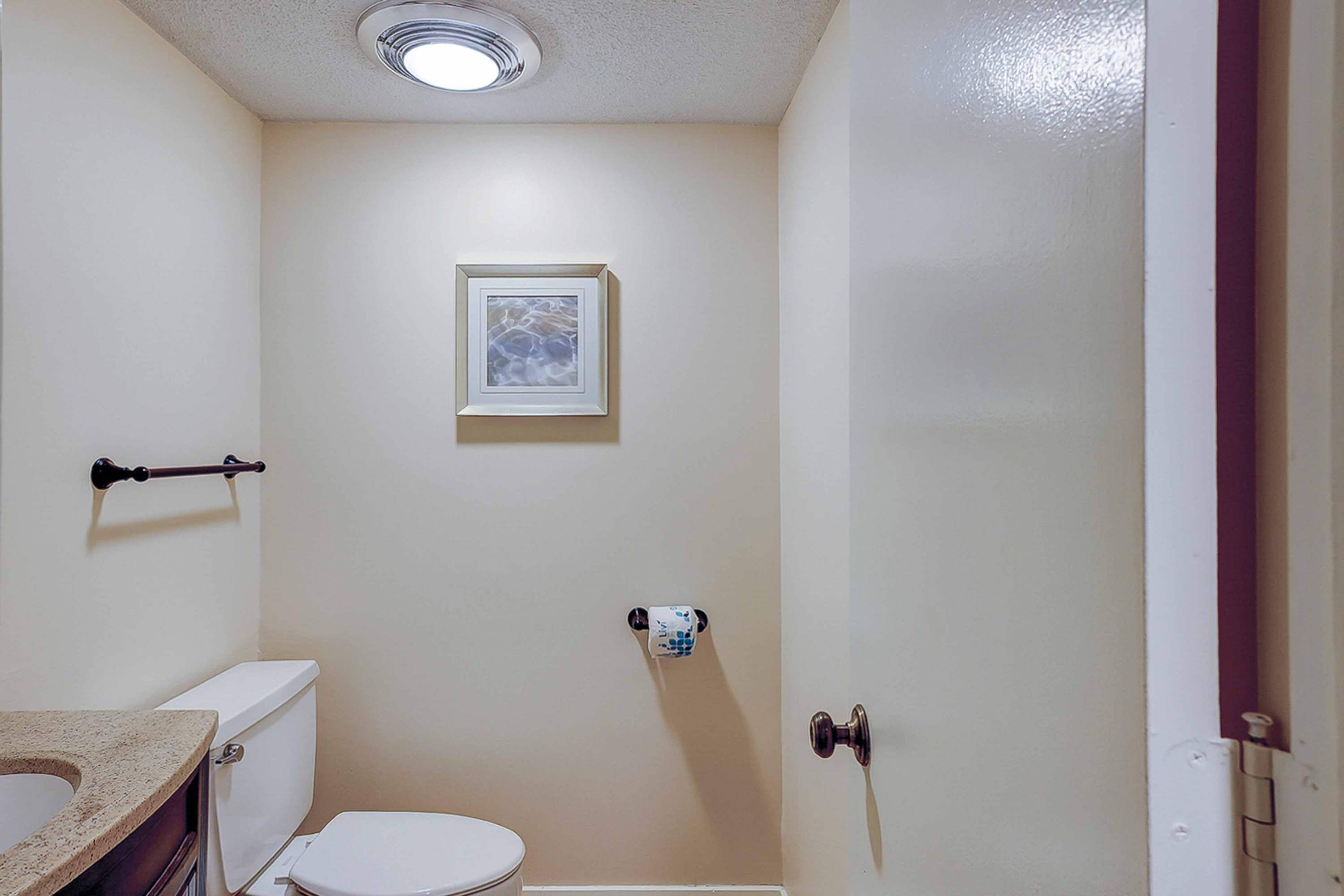 A small bathroom with a toilet, a sink, a towel rack, a framed picture on the wall, and a door.