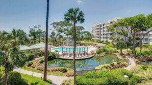 A resort with a central pool, surrounding lounge chairs, and a building with multiple balconies. - Beach dream with balcony view & shared pool, just steps away from the beach (Hilton Head)