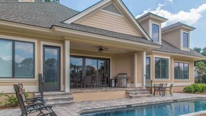 Una casa con piscina, mobili da patio e una zona esterna coperta con barbecue.