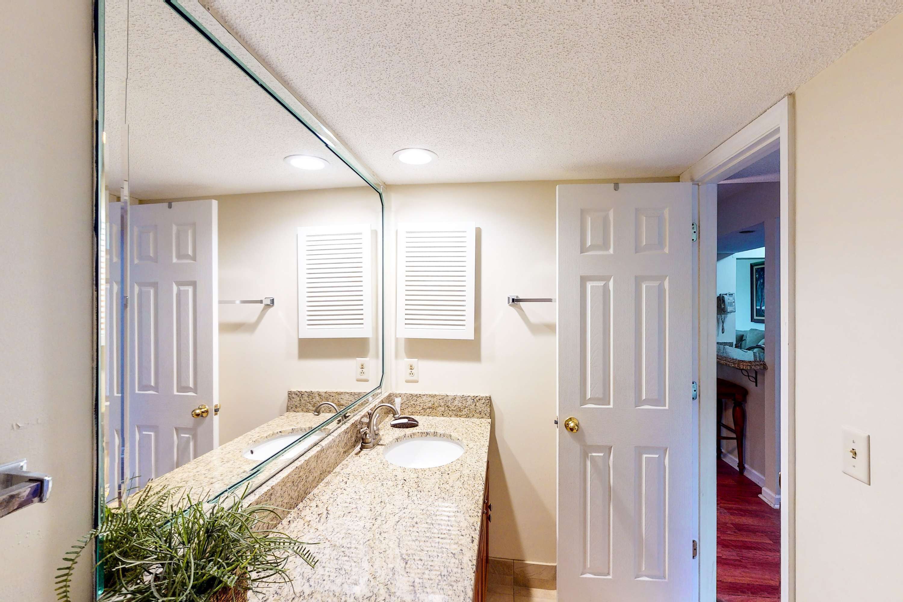 A bathroom with a double sink, a large mirror, and a potted plant.