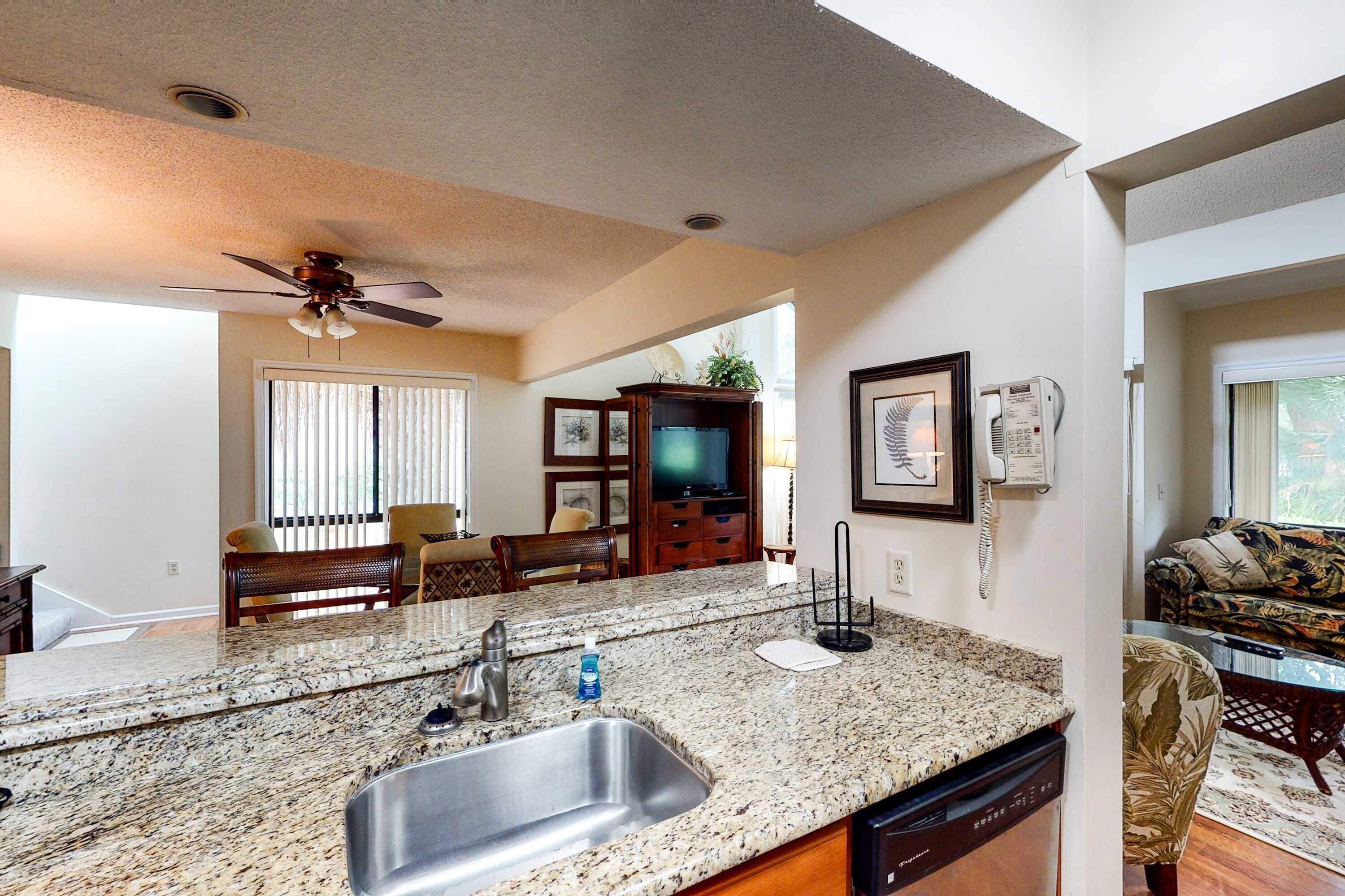 A kitchen with granite countertops, a stainless steel sink, a ceiling fan, and a dining area with a wooden table and chairs.