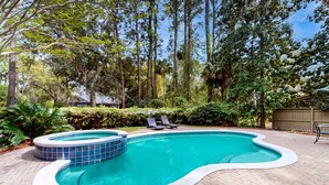 Piscina com hidromassagem, rodeada por um pátio de tijolos, árvores e duas espreguiçadeiras.