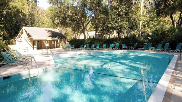 Una piscina con sillas de descanso, una torre de salvavidas y un edificio con tejado inclinado.