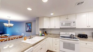 Una cocina con armarios blancos, microondas, horno, fregadero y comedor con sillas.