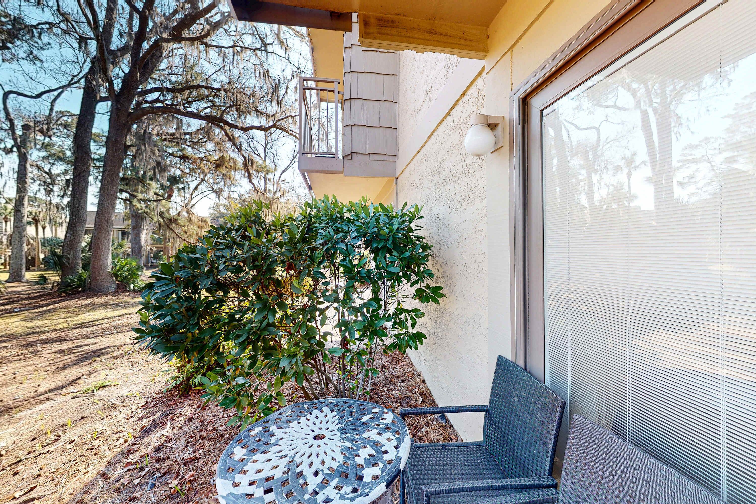 A patio with a round table and chairs, a small bush, and a garage door.