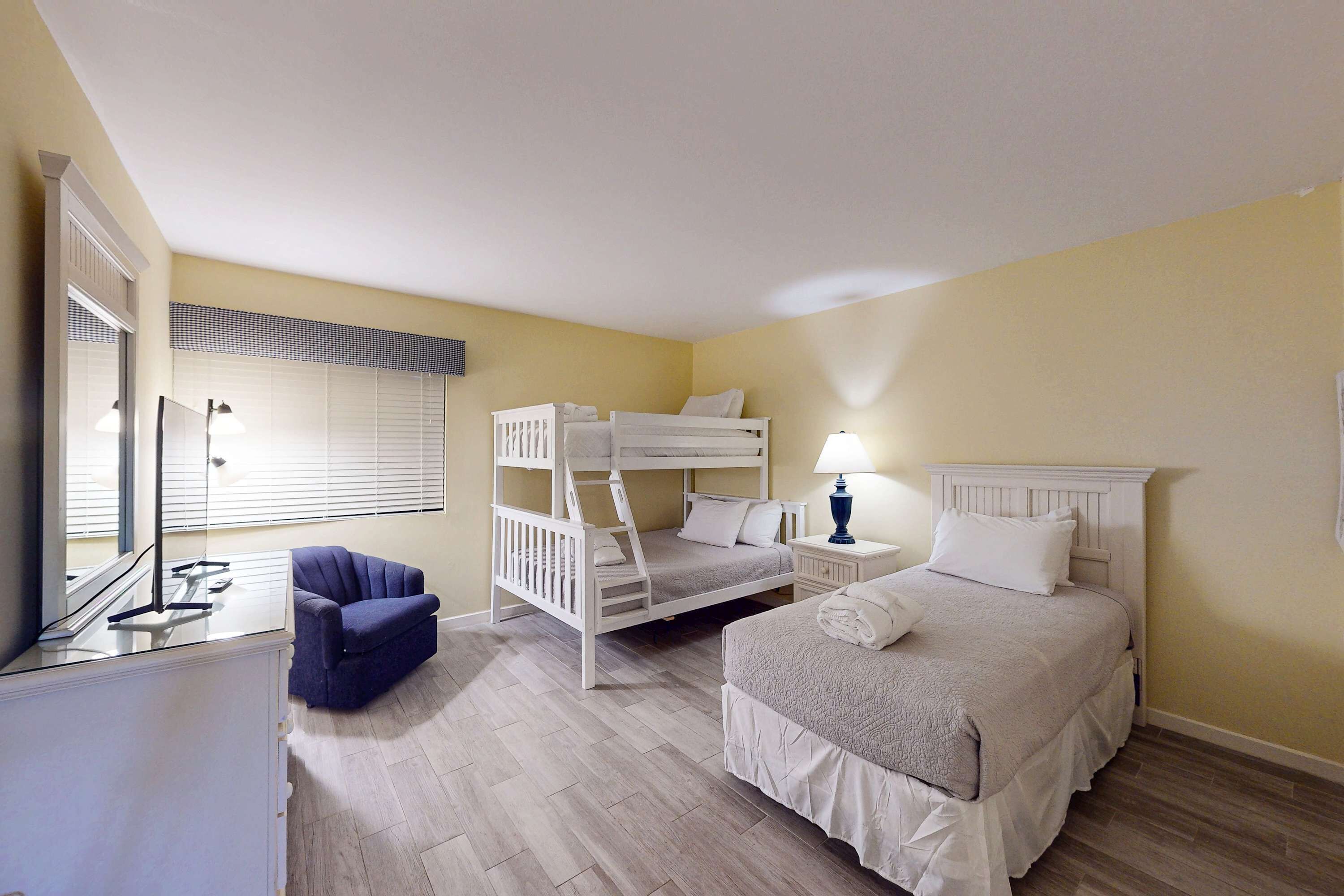 A bedroom with a bunk bed, a single bed, a chair, a desk, and a lamp.