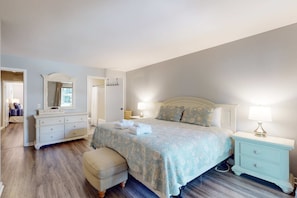 A bedroom with a bed, bedside tables, a dresser, a mirror, and an ottoman. - Snow Bird Friendly, ground floor island gem with pool access walk to beach (Hilton Head)