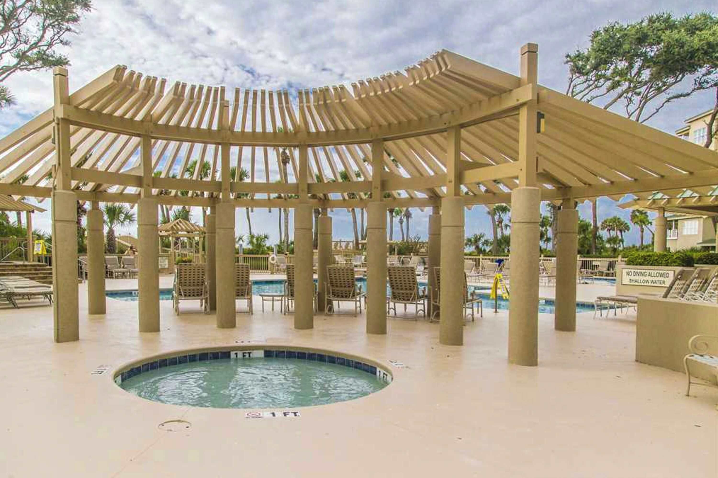 A covered pool area with lounge chairs, a hot tub, and a sign indicating no diving allowed.