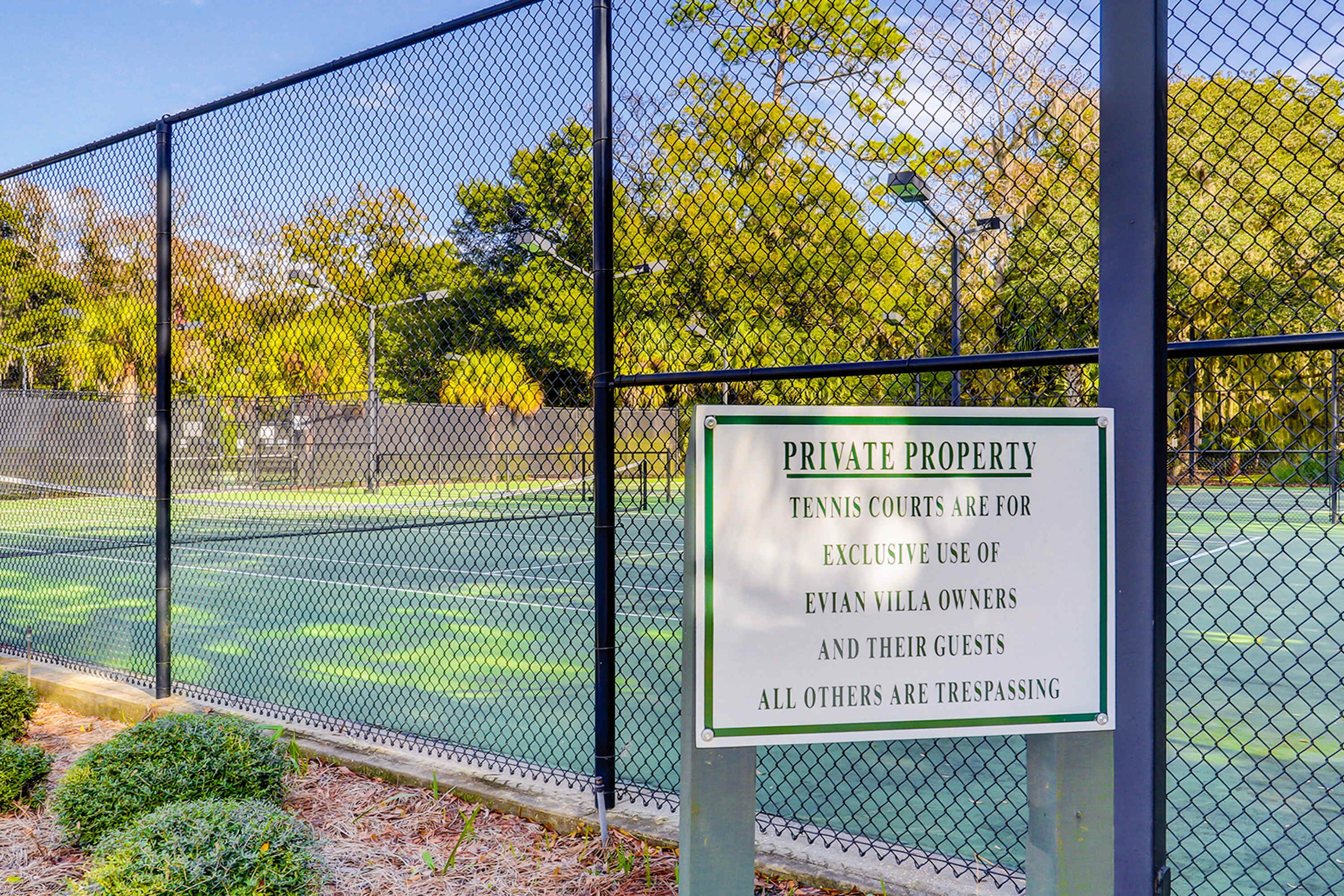 Un campo da tennis circondato da una recinzione a rete metallica, con un cartello che indica proprietà privata ad uso esclusivo dei proprietari Evan Vella e dei loro ospiti.