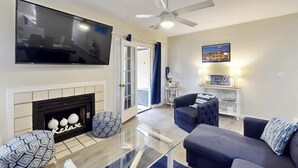 A living room with a flat-screen TV, a fireplace, a ceiling fan, and a sofa. - Charming French Inspired Villa, Dog Friendly Retreat with Patio, Pool & Tennis (Hilton Head)