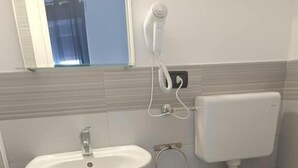 Een badkamer met een wastafel op een zuil, toilet en een klein houten plankje met toiletartikelen.