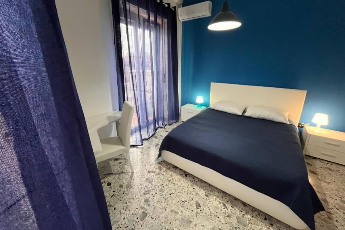 Une chambre à coucher comprenant un lit, un bureau, une chaise, une table de chevet et une lampe.